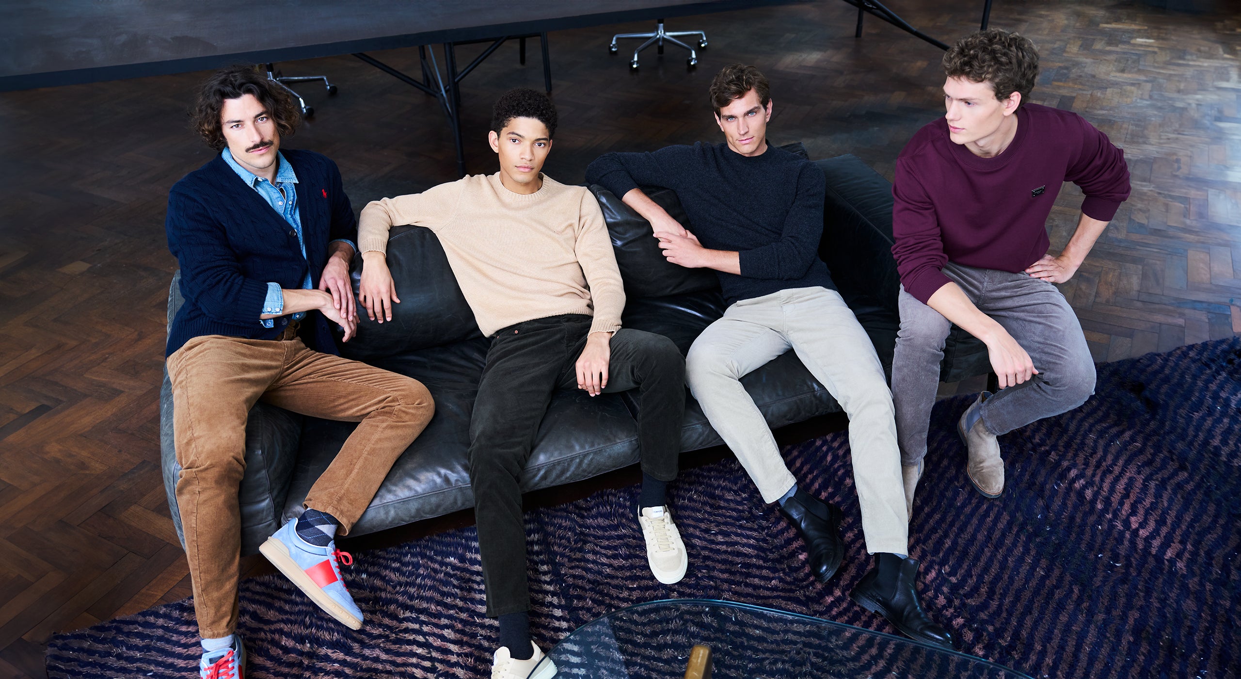 Four men sitting on a black leather couch in a modern interior setting.